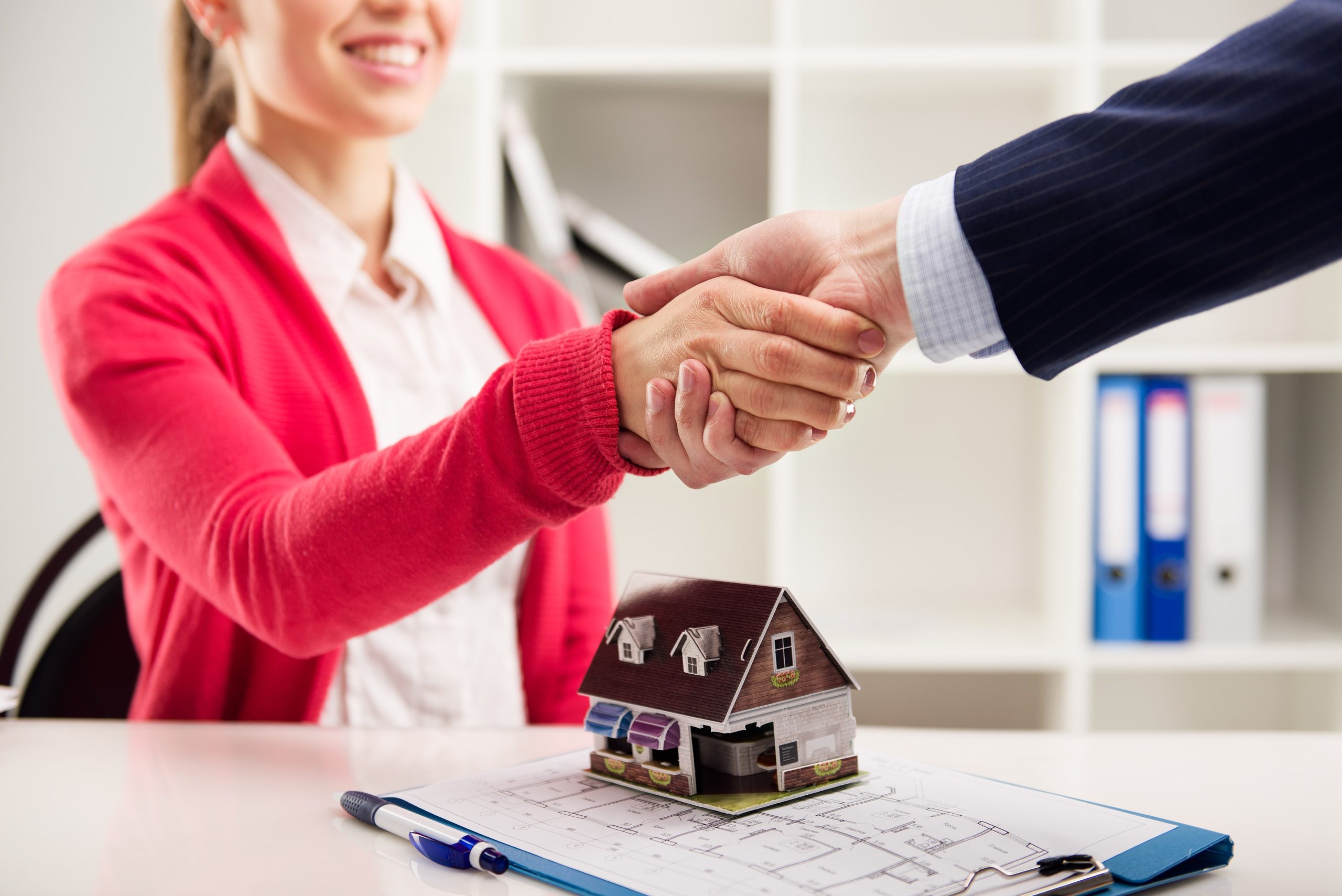 Two business people shaking hands as successful agreement in real estate agency office